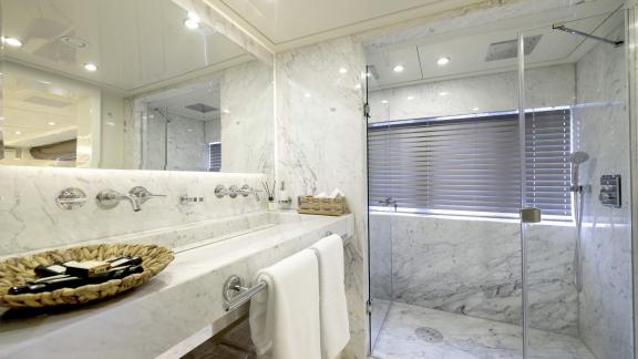 The marble bathroom with shower, washbasin and large mirror is brightly lit.